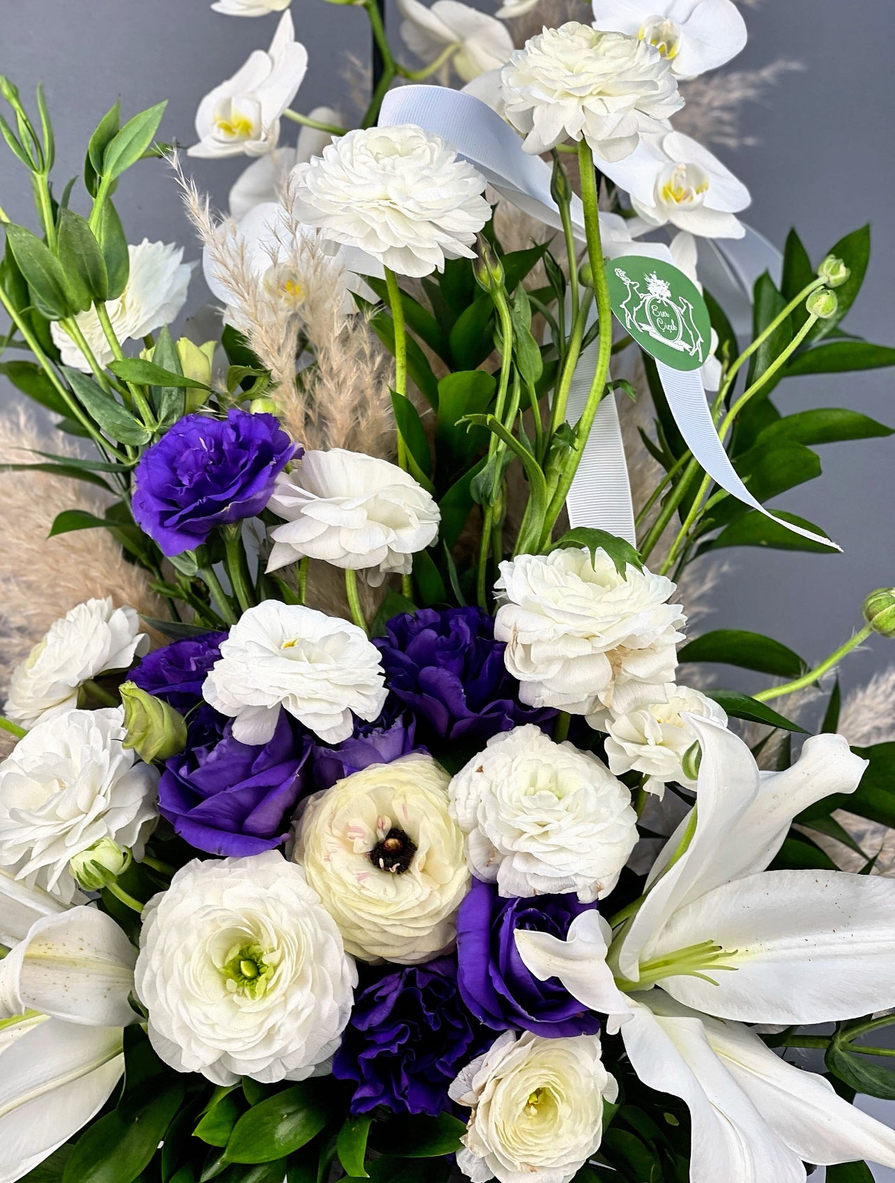 Çiçeklerin dingin kontrastı ve eskitme seramik vazonun sofistike birleşimi, aranjmanın huzur veren atmosferini vurguluyor.