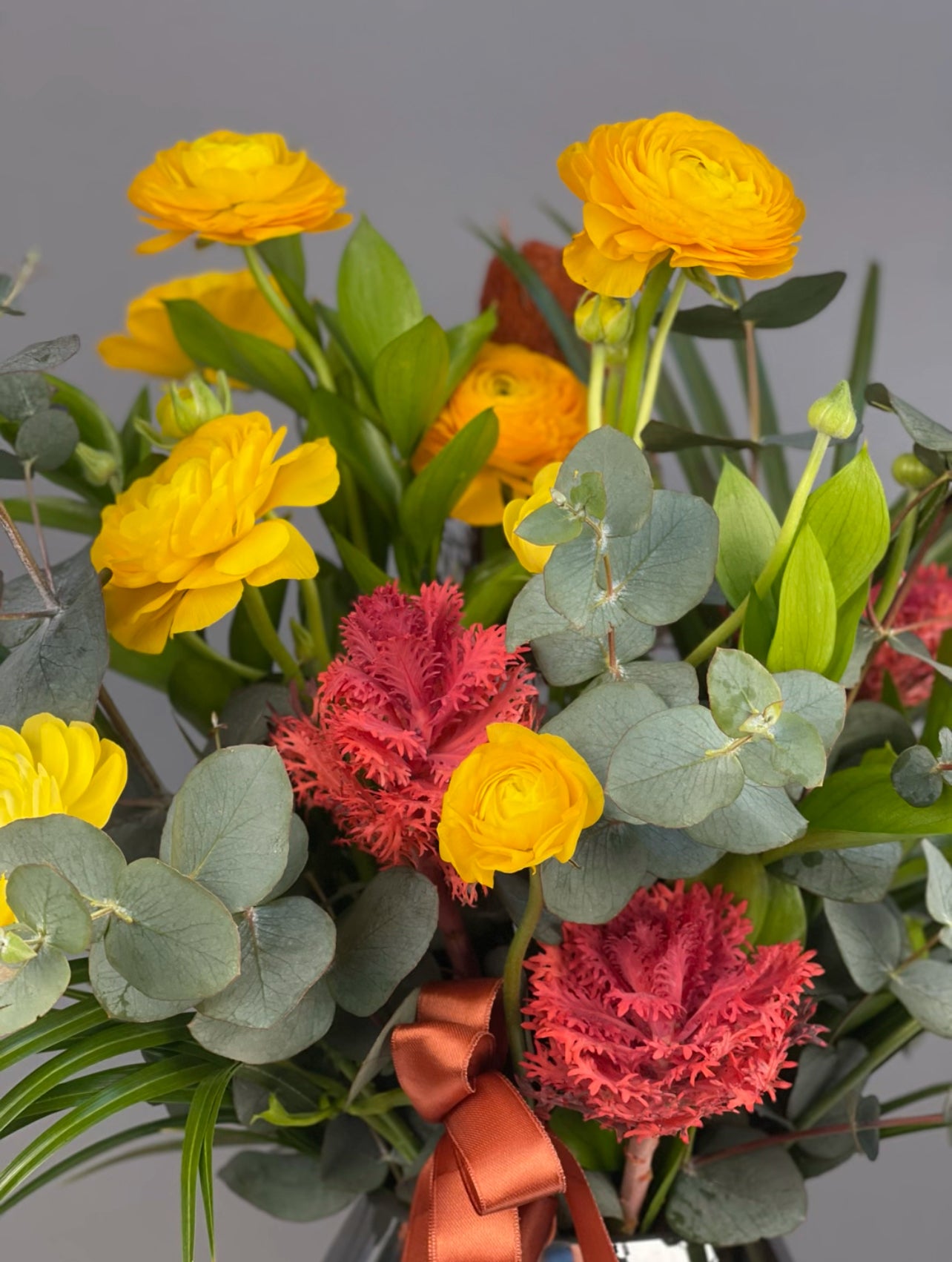 Modern dokunuşuyla canlı renklerin uyumunu yansıtan Deluxe Cam Vazoda Golden Crimson Medley aranjmanı, sarı erengül ve kırmızı lahananın estetik kombinasyonunu sergiliyor.