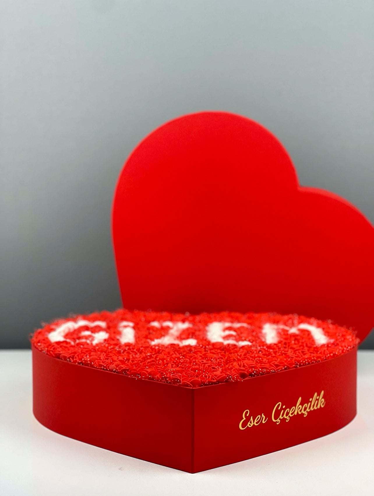 Grande boy kırmızı kalp kutunun yandan görünümünde kırmızı güller ve beyaz isim tasarım detayı