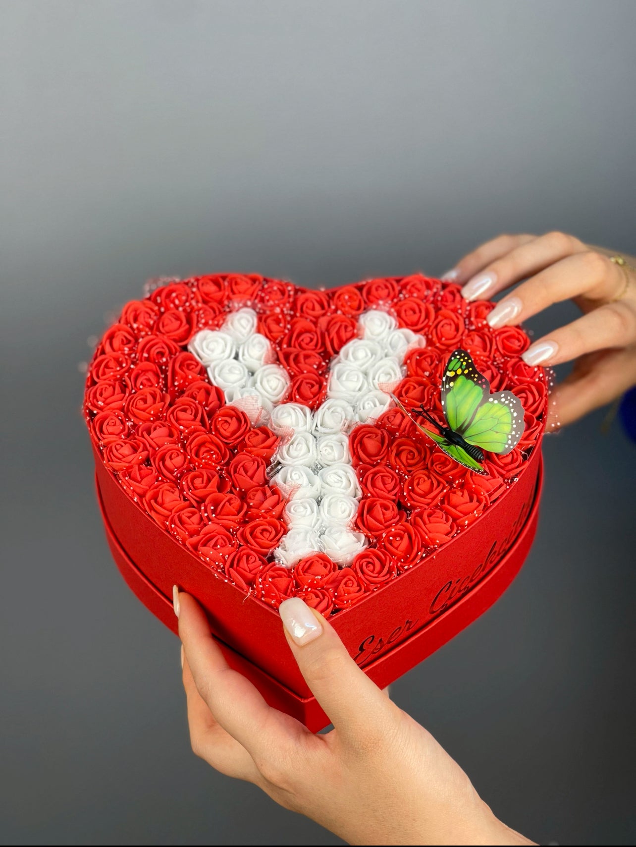 Petite boy kırmızı kutunun yandan görünümünde kırmızı güller ve beyaz güllerle oluşturulmuş harf tasarımı detayı