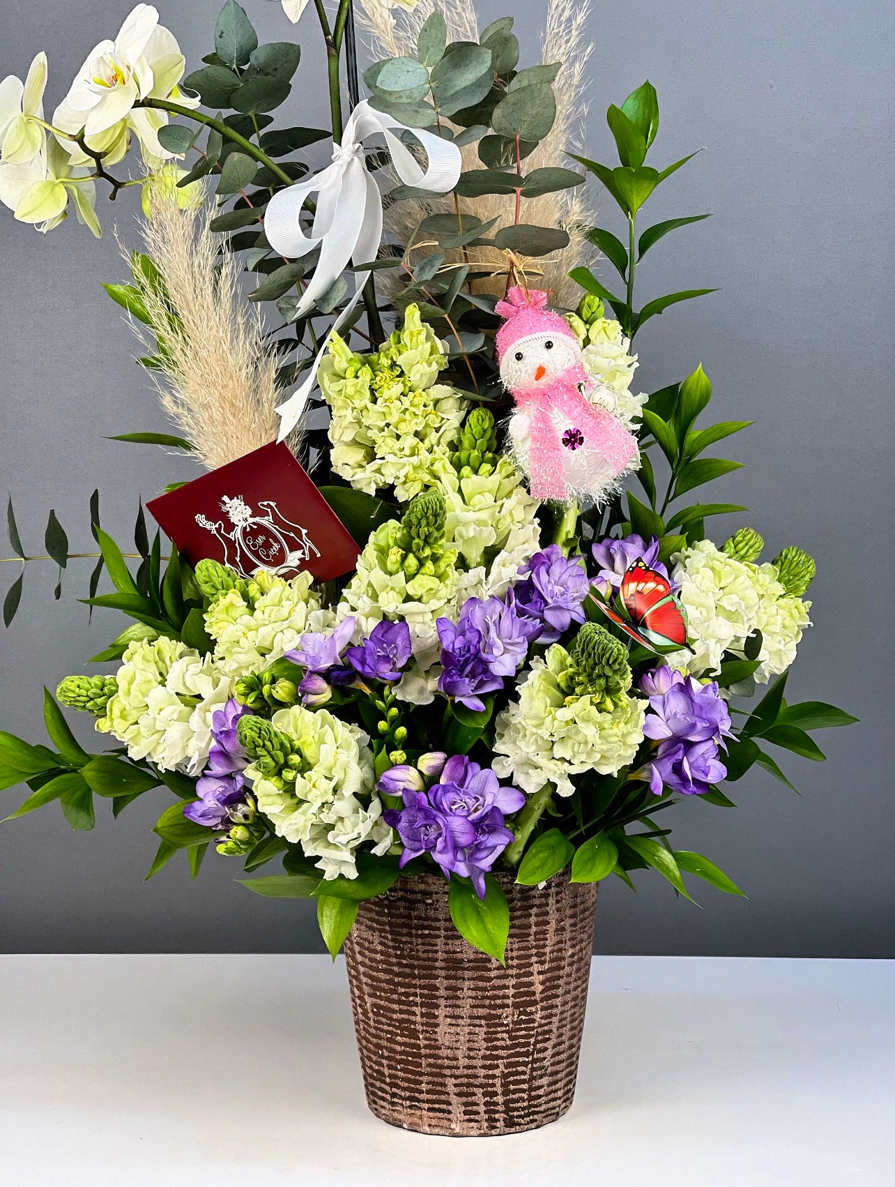 Aranjmanın genel görünümünde, çiçeklerin zarif uyumu ve vazonun rustik estetiği ön planda.