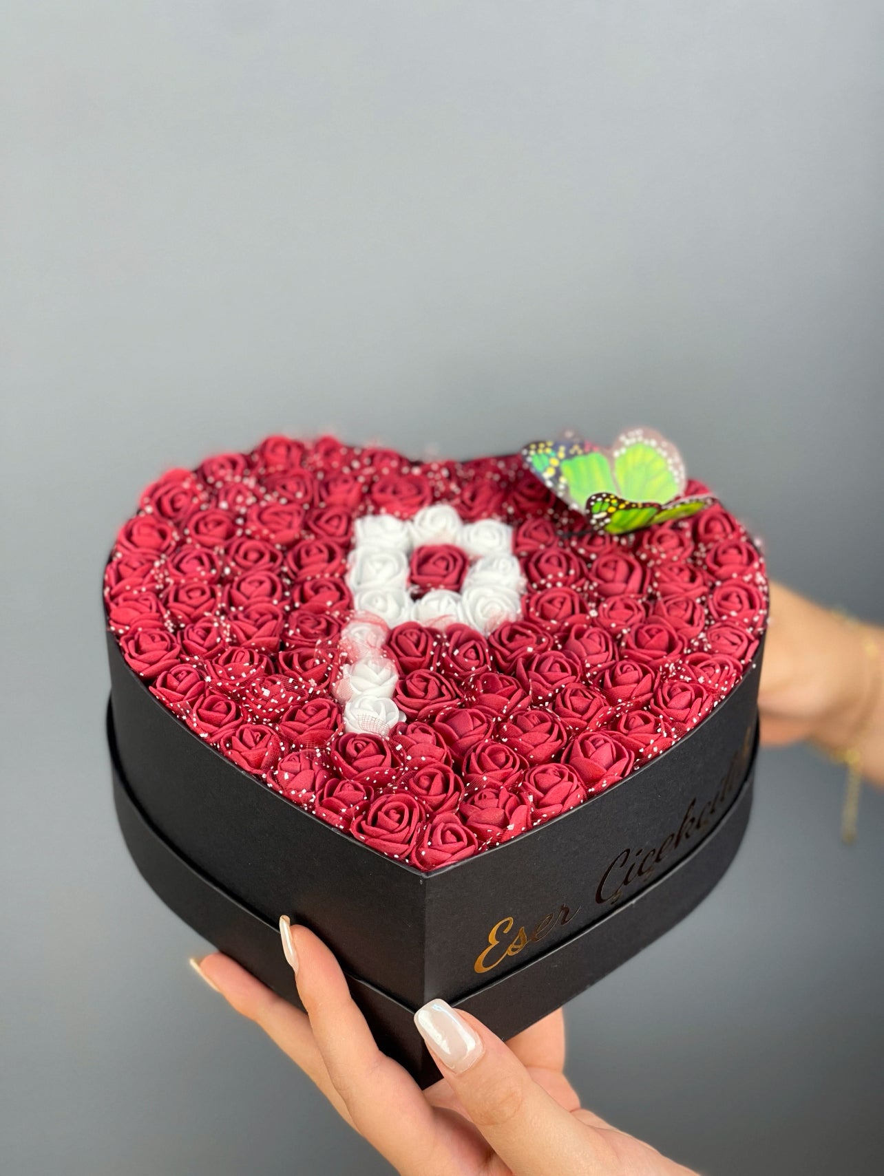 Üstten bakışta 20 cm siyah kalp kutuda bordo ve beyaz güllerle yapılmış harf tasarım düzeni