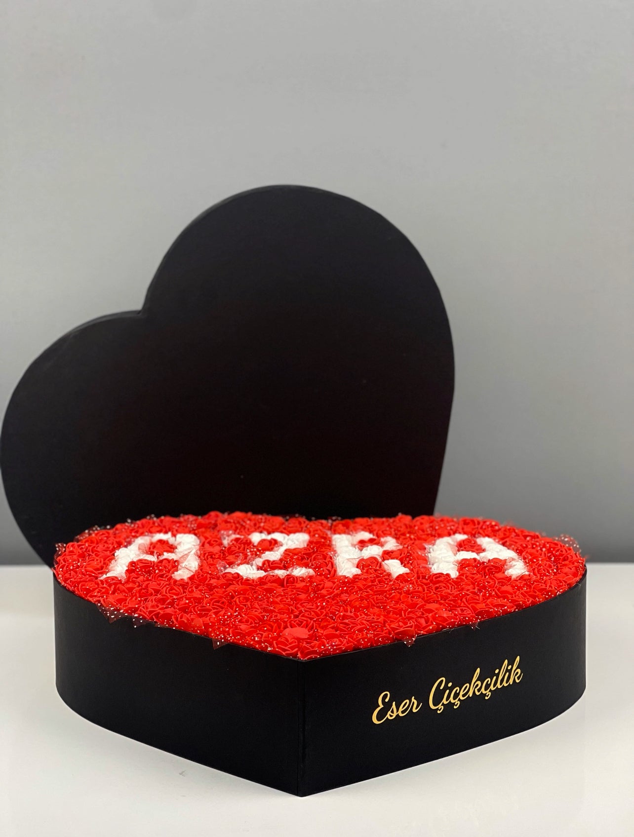 Grande boy siyah kutunun yandan görünümünde kırmızı güller ve beyaz isim tasarım detayı