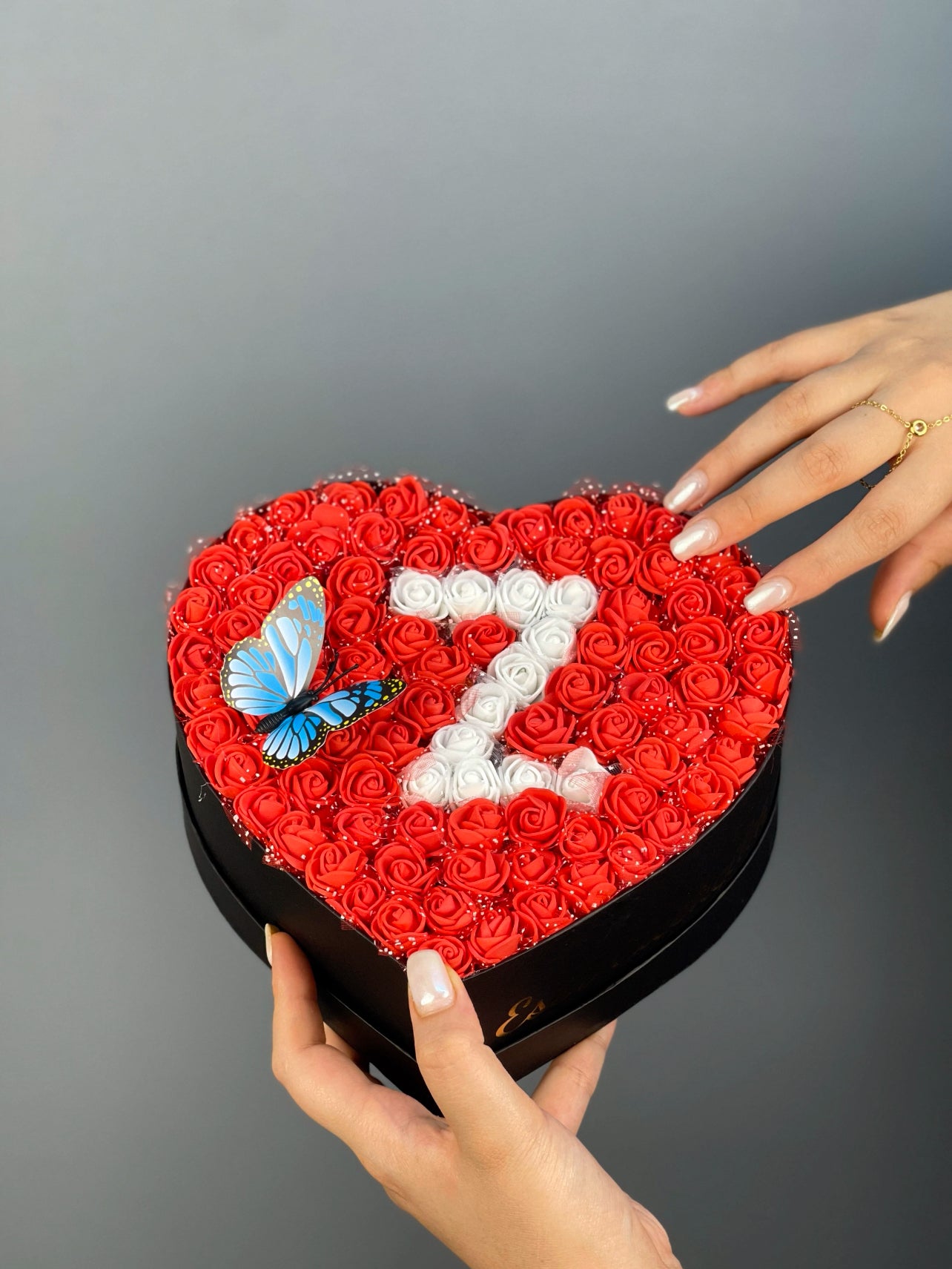 Üstten bakışta 20 cm siyah kalp kutuda kırmızı ve beyaz güllerle yapılmış harf tasarım düzeni