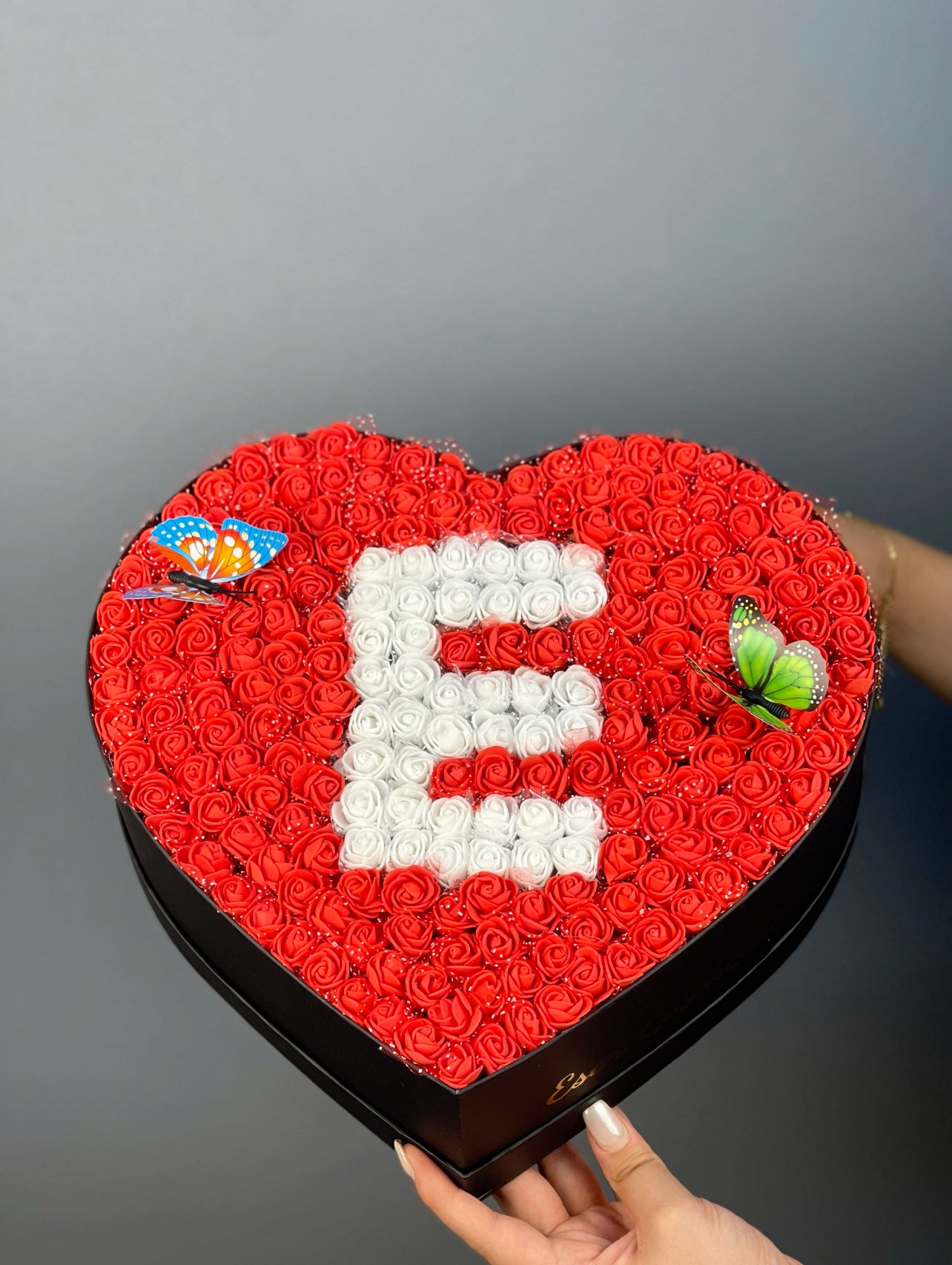 Classic boy siyah kutunun yandan görünümünde kırmızı güller ve beyaz güllerle oluşturulmuş harf tasarımı detayı