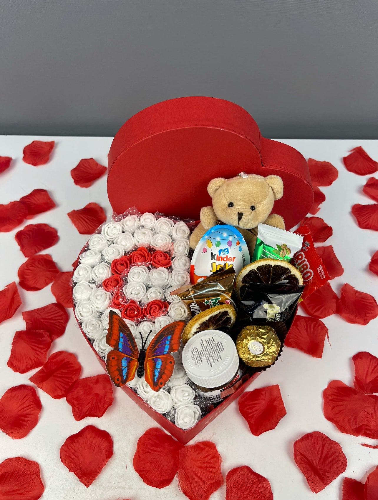 Kırmızı kutunun yandan görünümü: güller, çikolatalar ve peluş oyuncak detaylı sunum.
