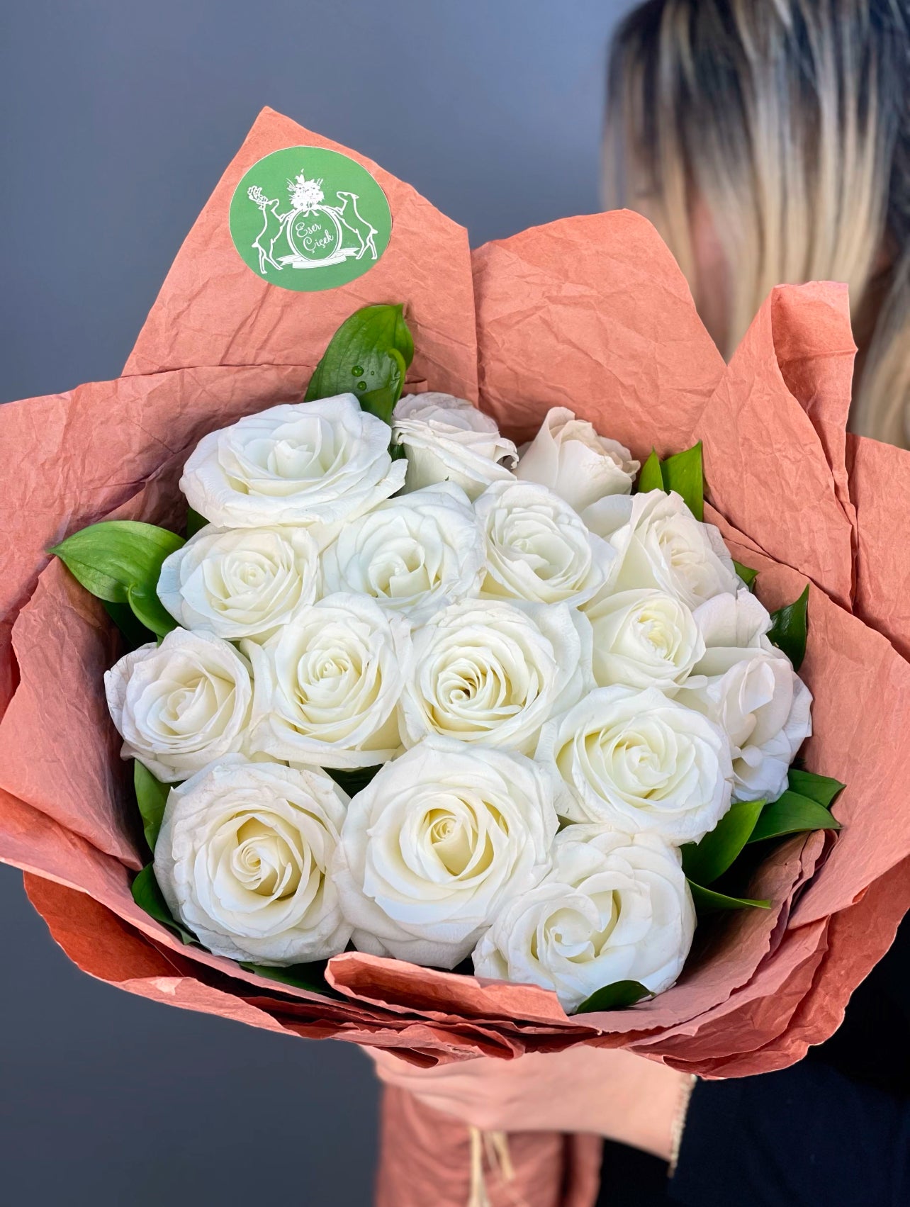 Beyaz güllerin asaleti ve ruskus yapraklarının doğal dokunuşuyla tamamlanan romantik buket.