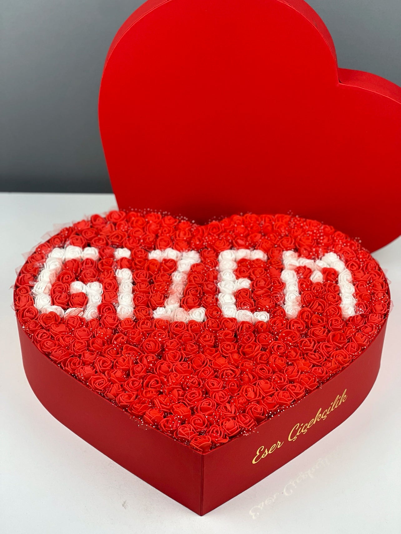 Kalp kutu içindeki kırmızı güller üzerine yerleştirilmiş beyaz isim tasarımının yakın çekim detayı
