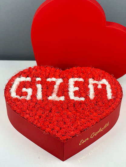 Kalp kutu içindeki kırmızı güller üzerine yerleştirilmiş beyaz isim tasarımının yakın çekim detayı