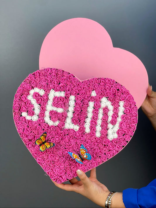 Grande boy pembe kalp kutuda fuşya güller üzerine beyaz güllerden yapılmış isim tasarımının ön cephe görünümü
