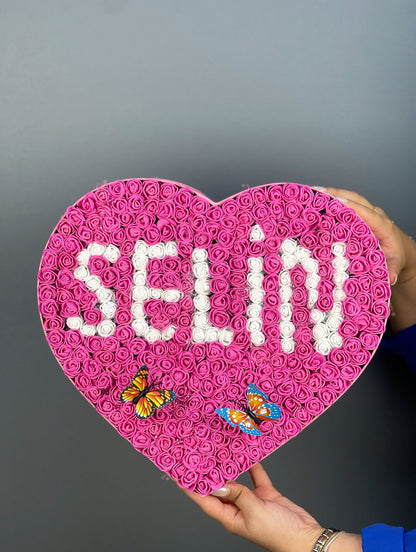 Grande boy pembe kutunun yandan görünümünde fuşya güller ve beyaz güllerle oluşturulmuş isim tasarımı detayı