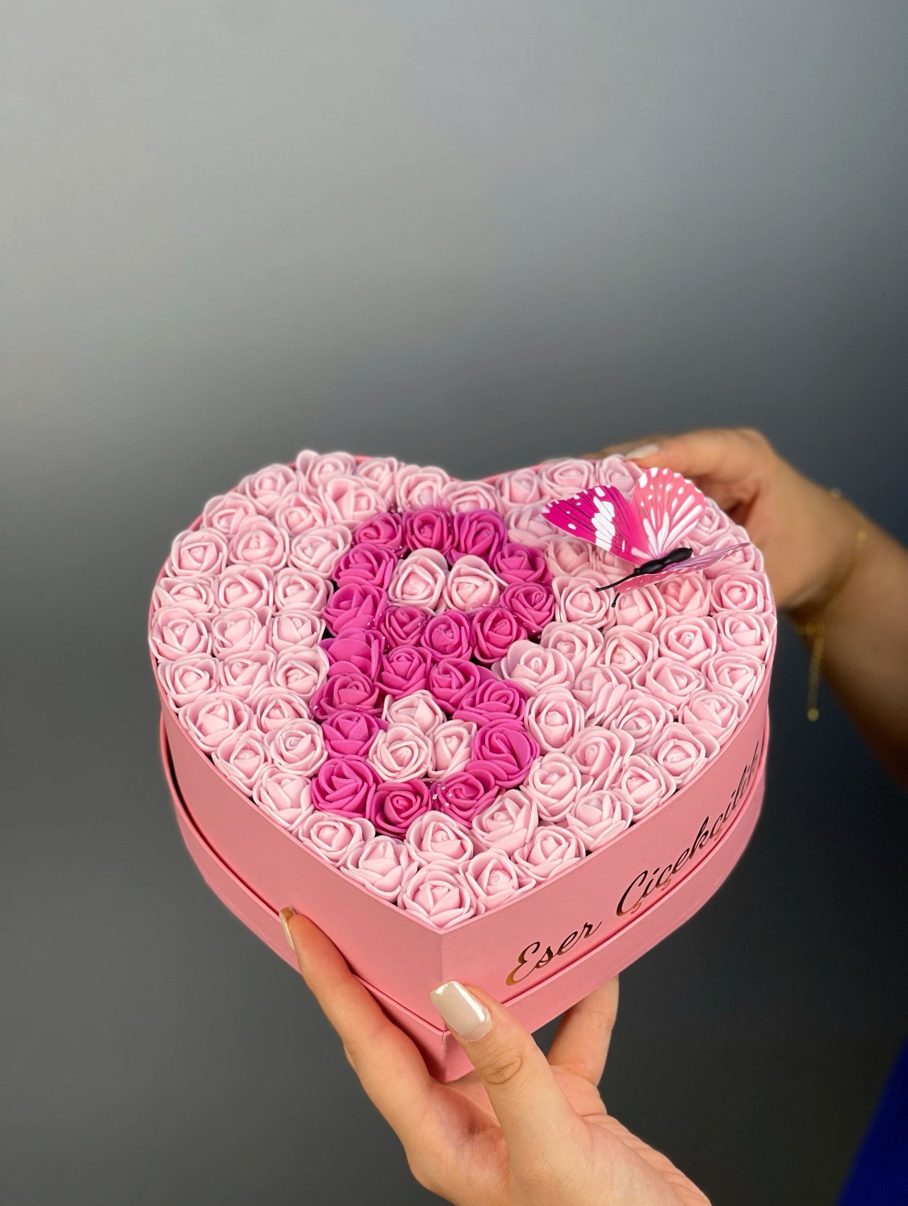 Üstten bakışta 20 cm pembe kalp kutuda pembe ve fuşya güllerle yapılmış harf tasarım düzeni
