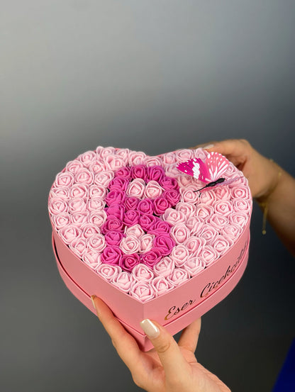 Üstten bakışta 20 cm pembe kalp kutuda pembe ve fuşya güllerle yapılmış harf tasarım düzeni
