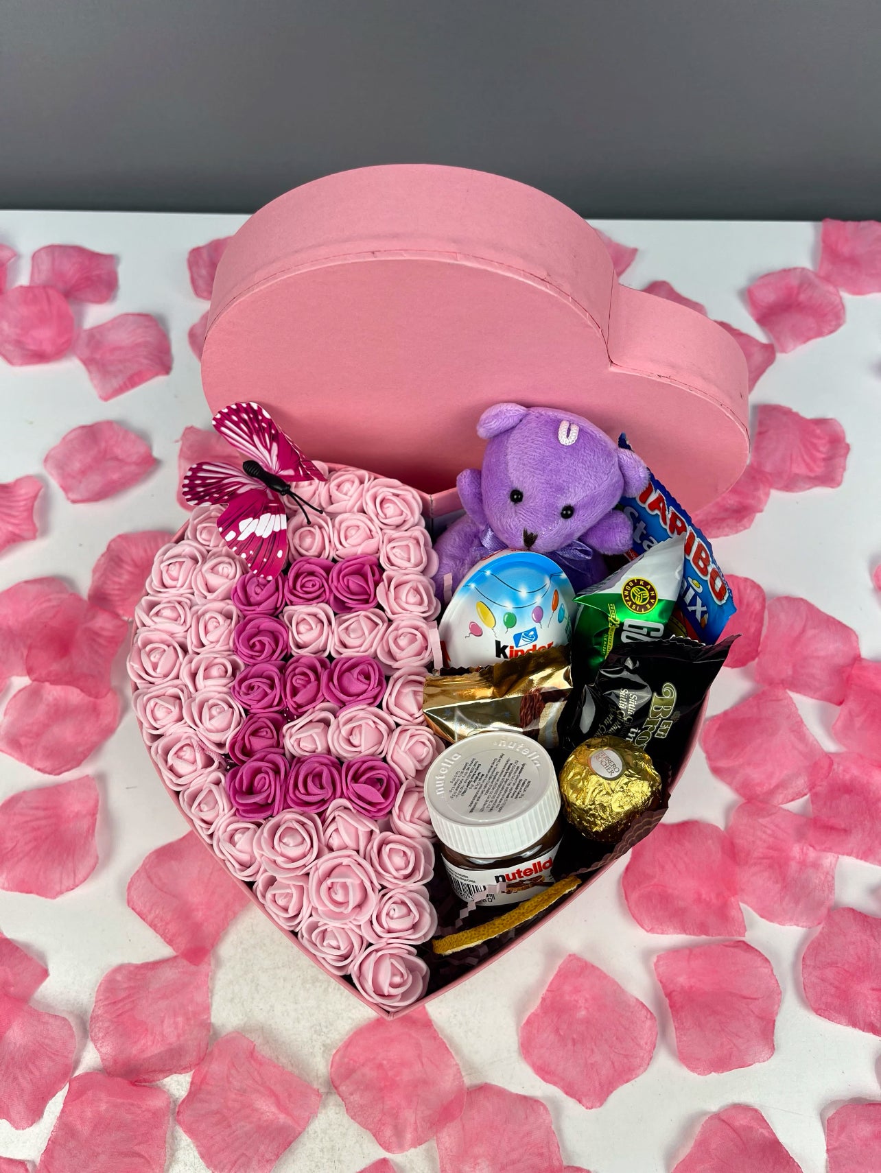 20×8 cm pembe kalp kutuda, yarısı çikolata ve peluş oyuncak, yarısı pembe ve fuşya güllerden harf tasarımıyla hazırlanan aranjman.
